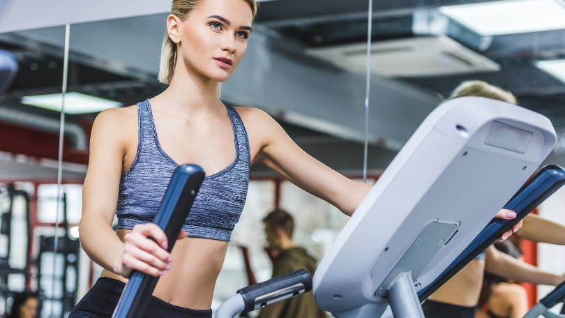 beautiful sportive woman working out on elliptical machine at gym